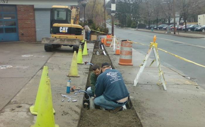 Workers digging a trench along a sidewalk